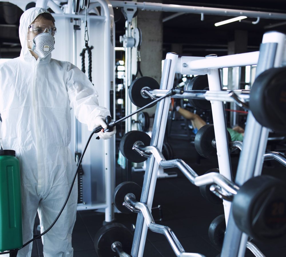 Man in white protection suit disinfecting and fitness equipment and weights to stop spreading highly contagious corona virus. Man in white protection suit disinfecting and fitness equipment and weights to stop spreading highly contagious corona virus.